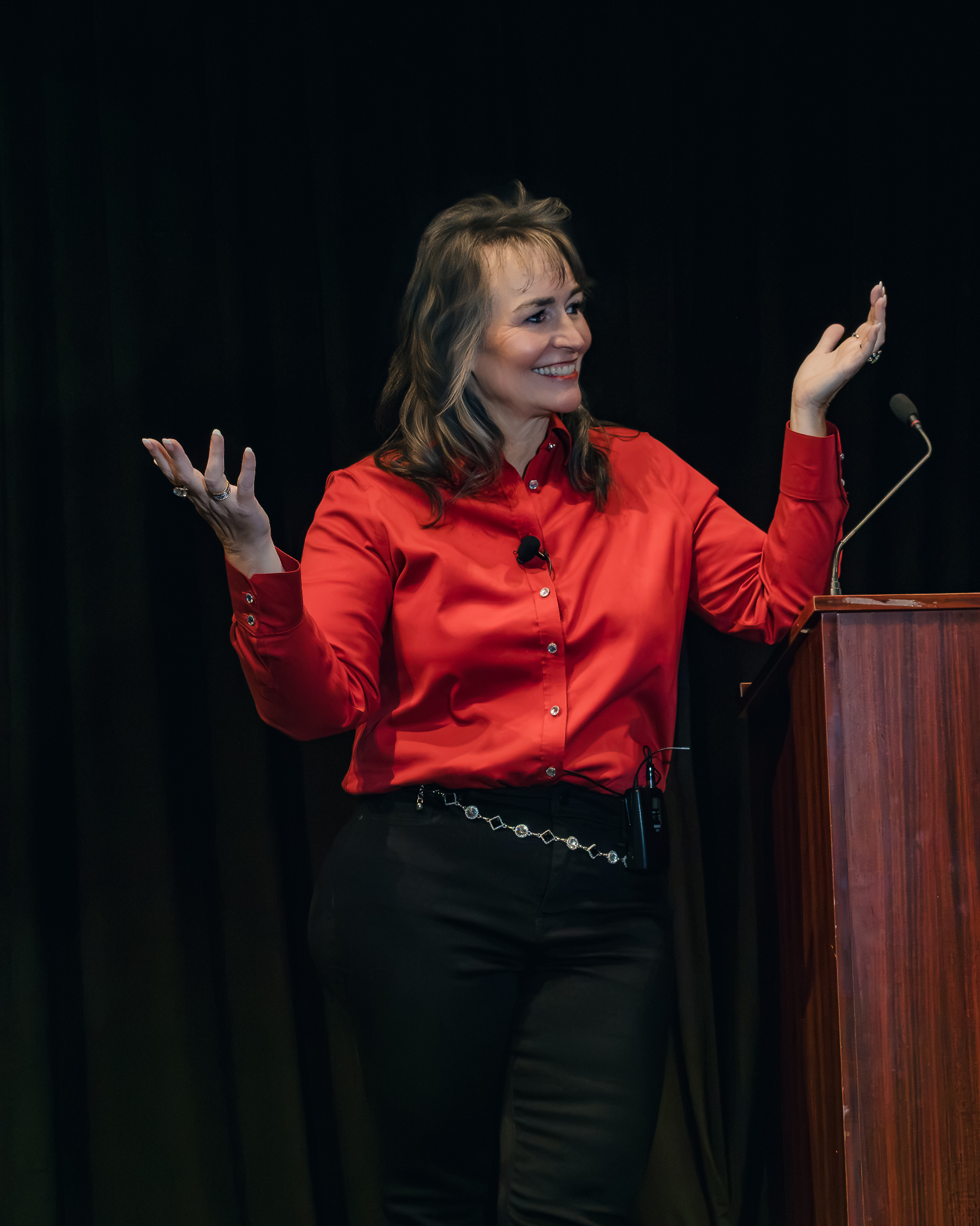 Kate Woodward Young with both hands raised, engaging an audience during a keynote